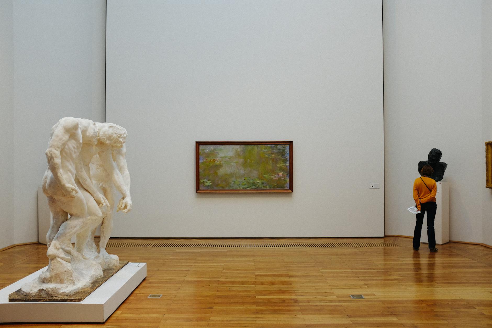 Impressionist paintings hung on the wall of a Paris museum gallery with visitors looking at them