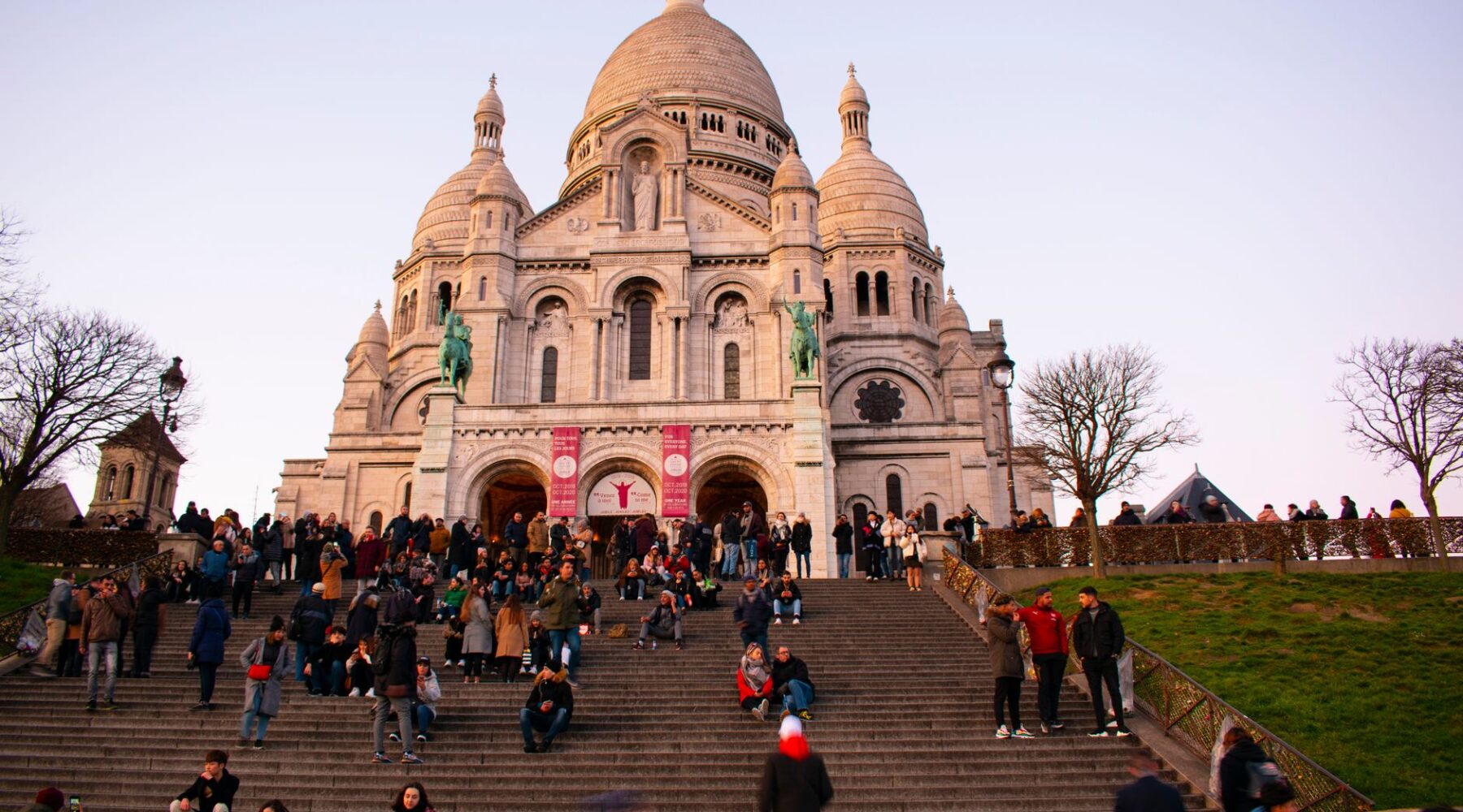 People sitting on the steps below the white domes of Sacre-Coeur in Montmartre at dusk