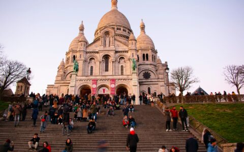 People sitting on the steps below the white domes of Sacre-Coeur in Montmartre at dusk