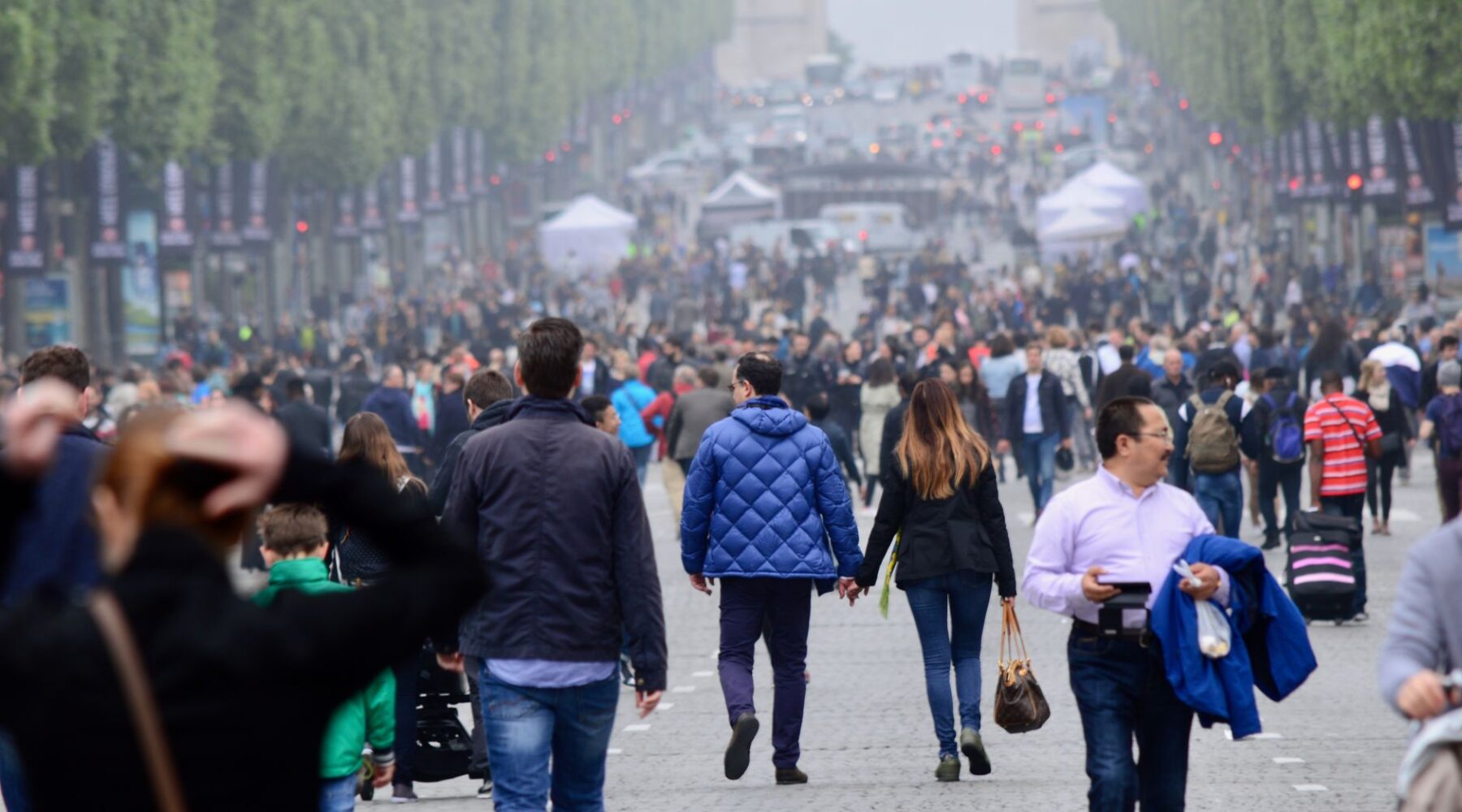 A dense crowd of pedestrians walking down a car-free Champs-Élysées towards the Arc de Triomphe in the haze