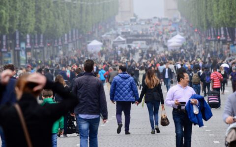 A dense crowd of pedestrians walking down a car-free Champs-Élysées towards the Arc de Triomphe in the haze