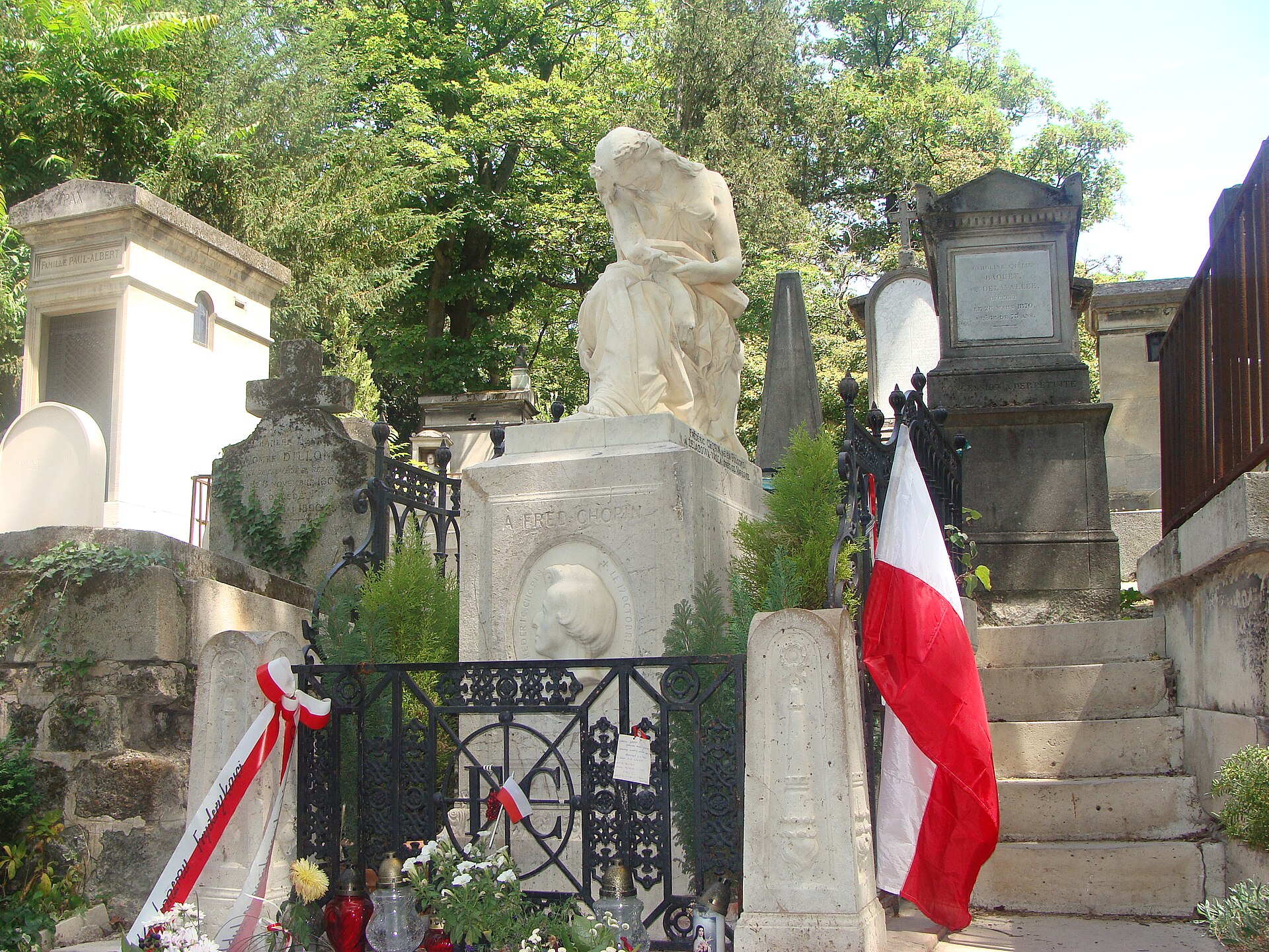 The white marble tomb of Frédéric Chopin at Père Lachaise, topped with a mourning muse and decorated with flowers and a red and white Polish flag