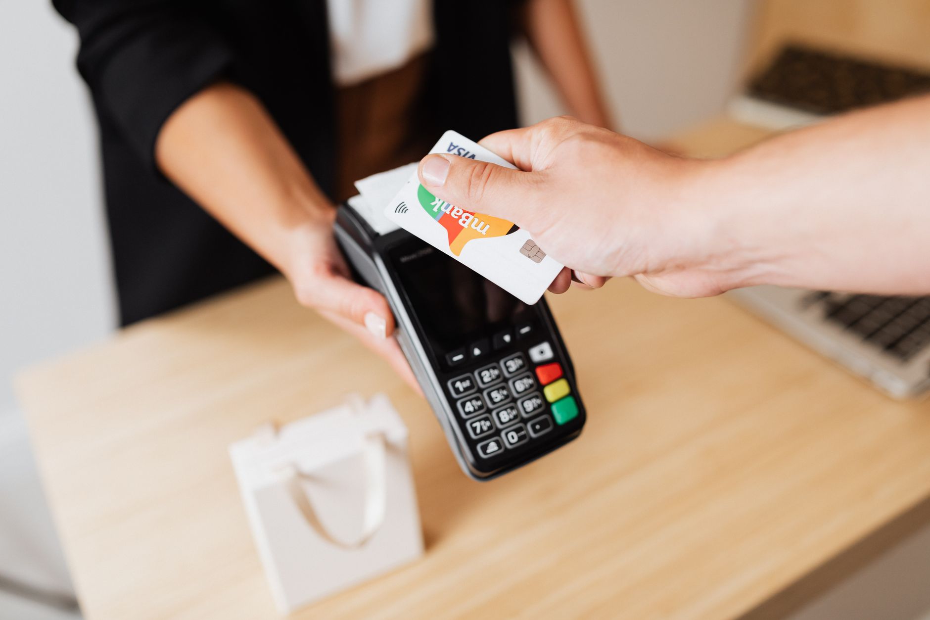 A customer holding a contactless bank card against a handheld card payment terminal at a shop counter