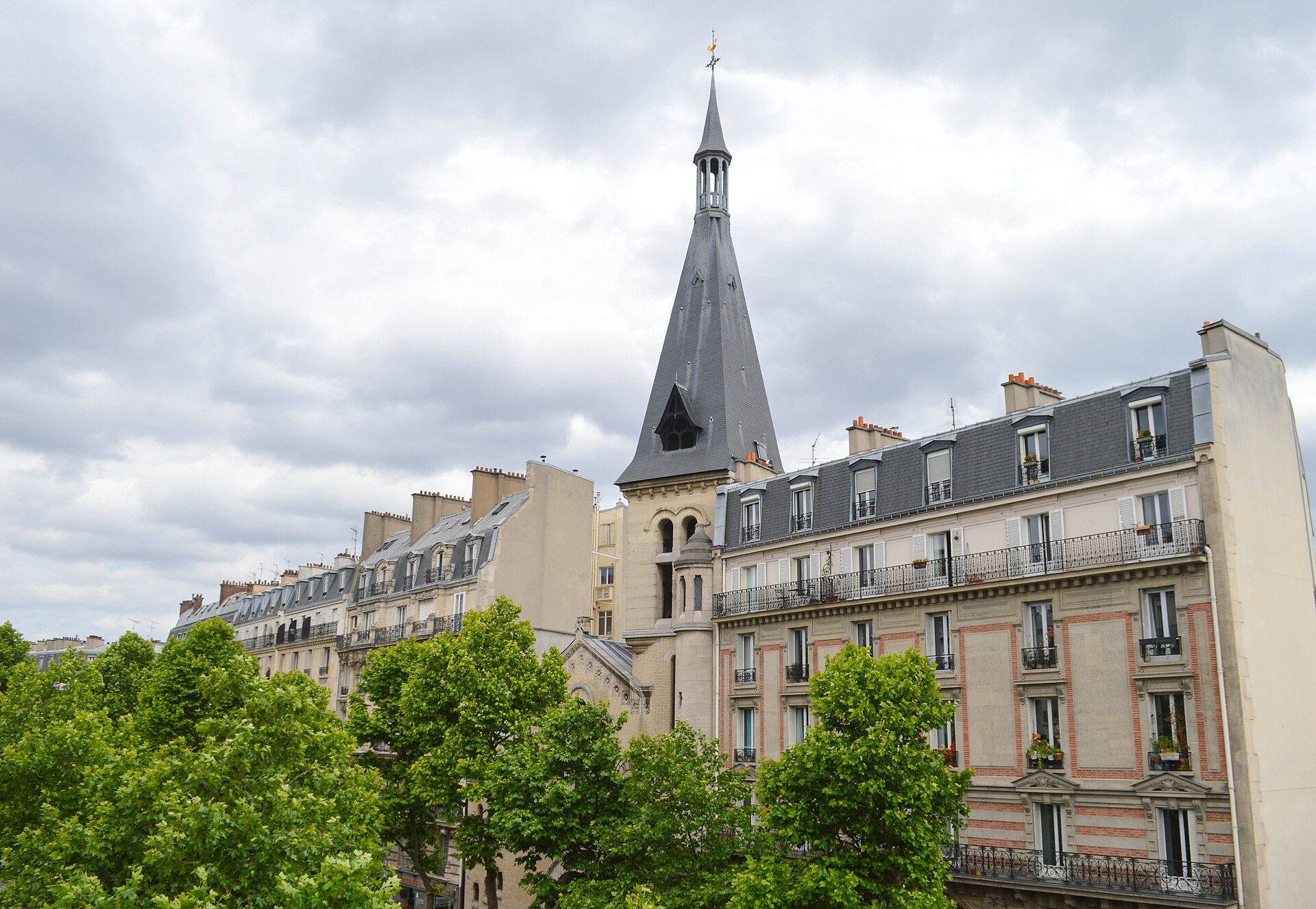 Rooftops, a church spire and Haussmann facades seen at tree level from the elevated Promenade plantee in eastern Paris