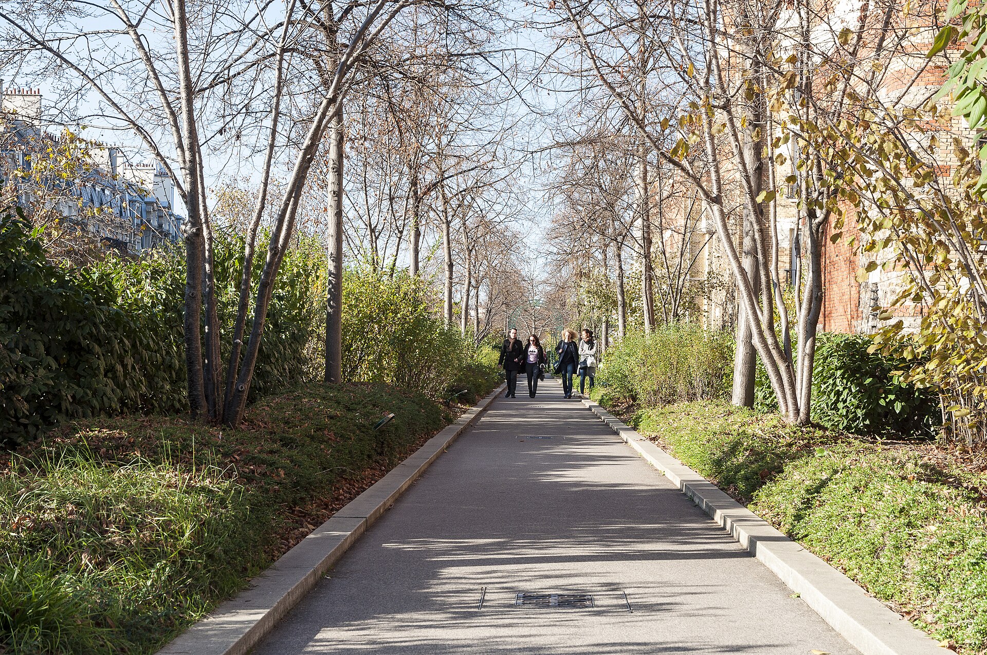 A paved path lined with young trees and planted borders running along the elevated Coulée verte René-Dumont, with Paris apartment buildings on the left
