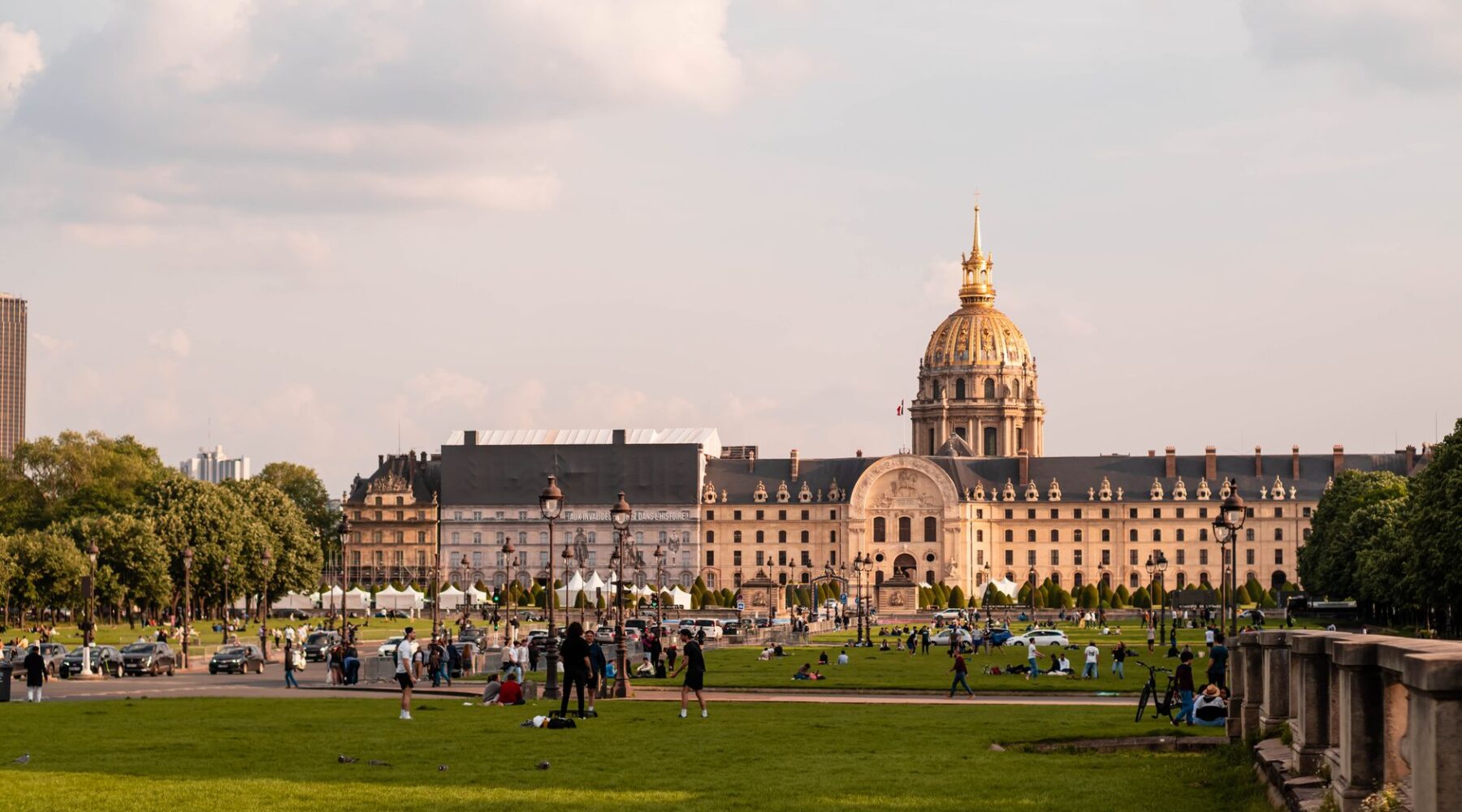 People relaxing and walking on the broad lawns of the Esplanade des Invalides in late afternoon light, with the golden dome of Les Invalides behind