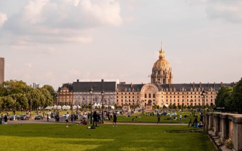 People relaxing and walking on the broad lawns of the Esplanade des Invalides in late afternoon light, with the golden dome of Les Invalides behind