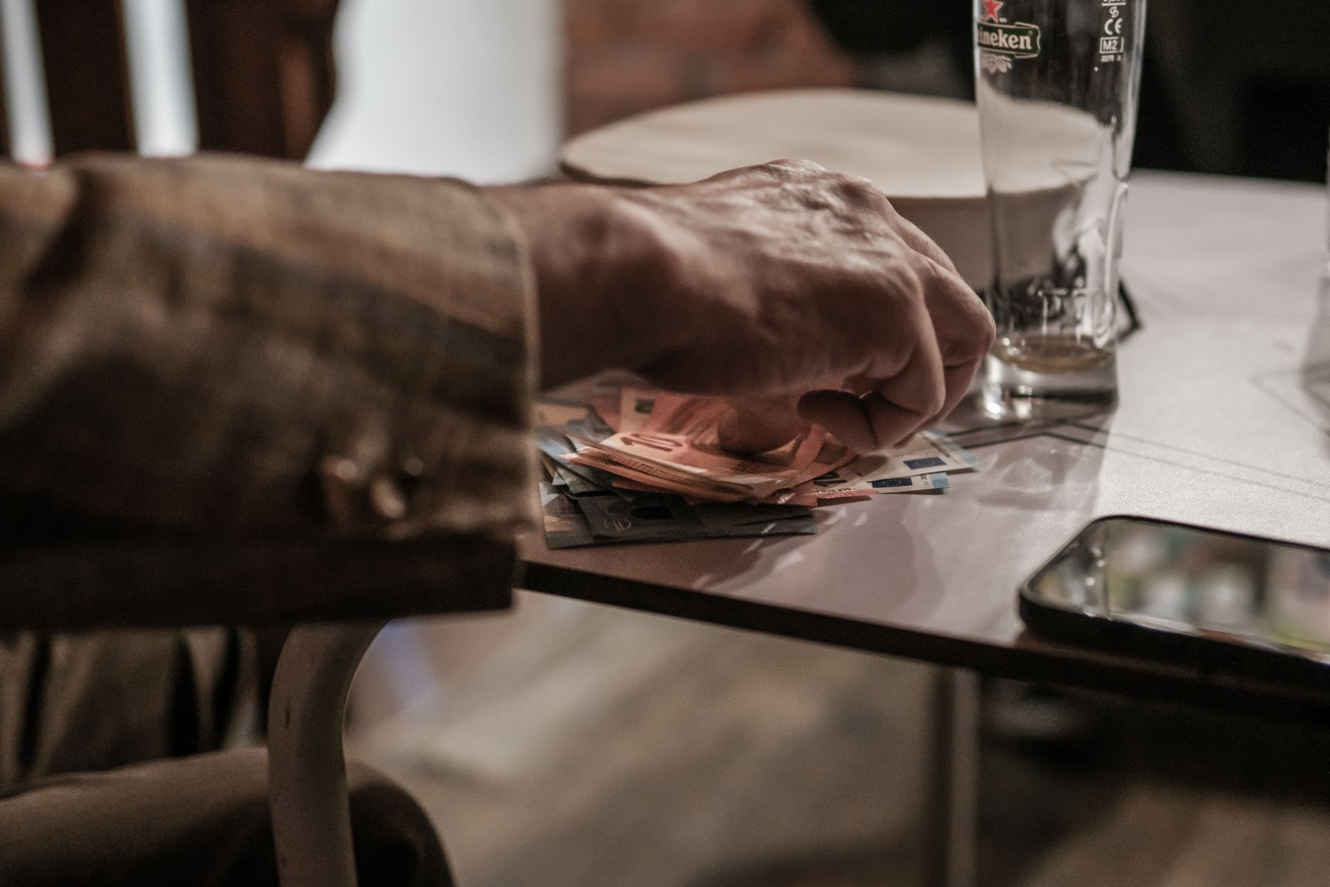 A hand laying euro banknotes on a small café table beside an empty glass