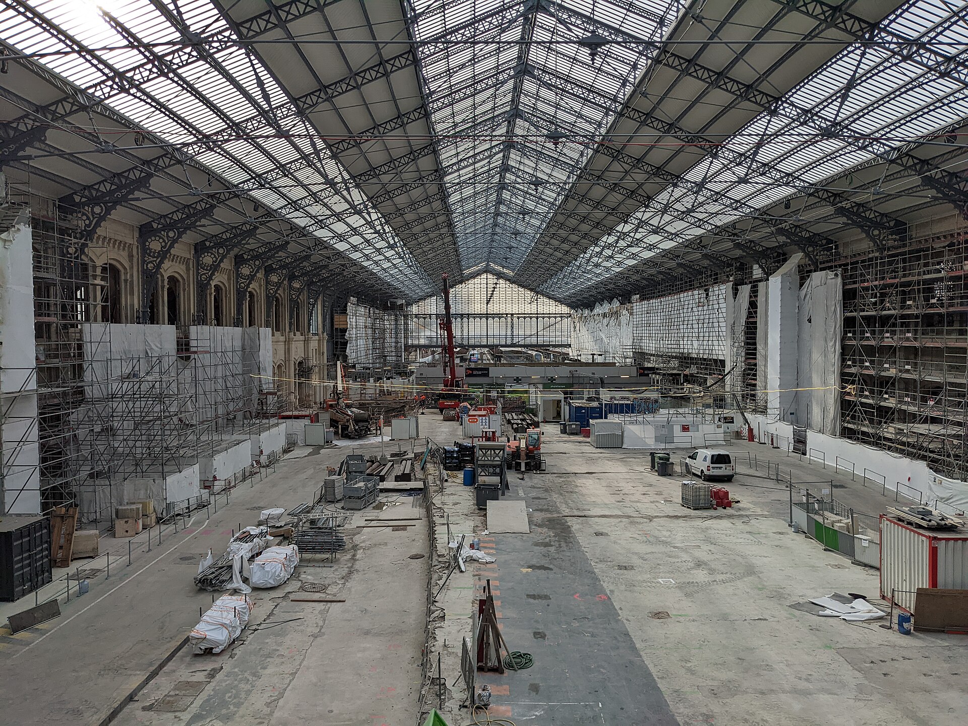The vast iron and glass roof of the Grande Halle at Gare d'Austerlitz above an empty construction site, with scaffolding along the walls