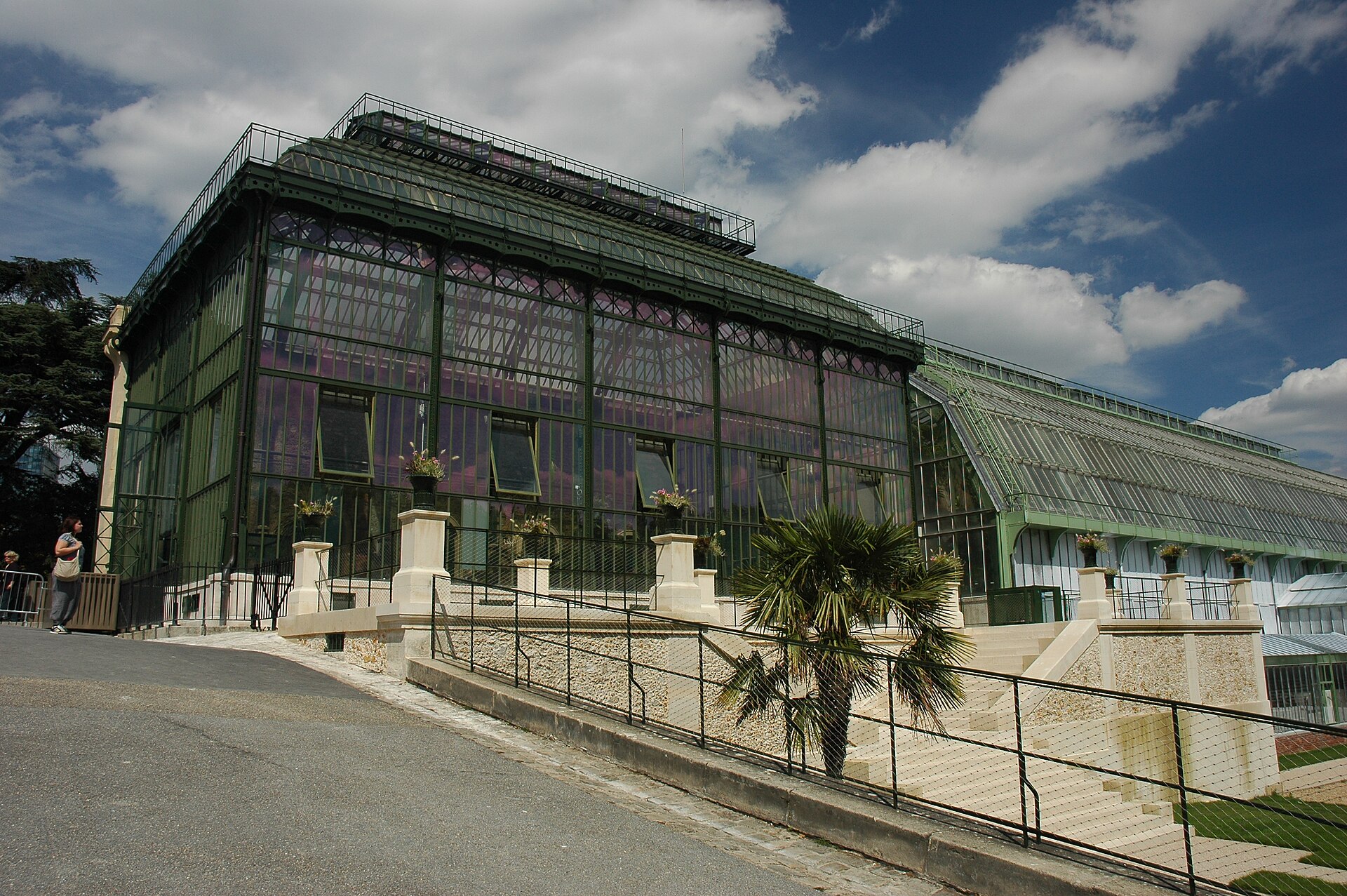 The large glass and iron Art Deco rainforest glasshouse of the Grandes Serres at the Jardin des Plantes, with a stone terrace and ramp in front