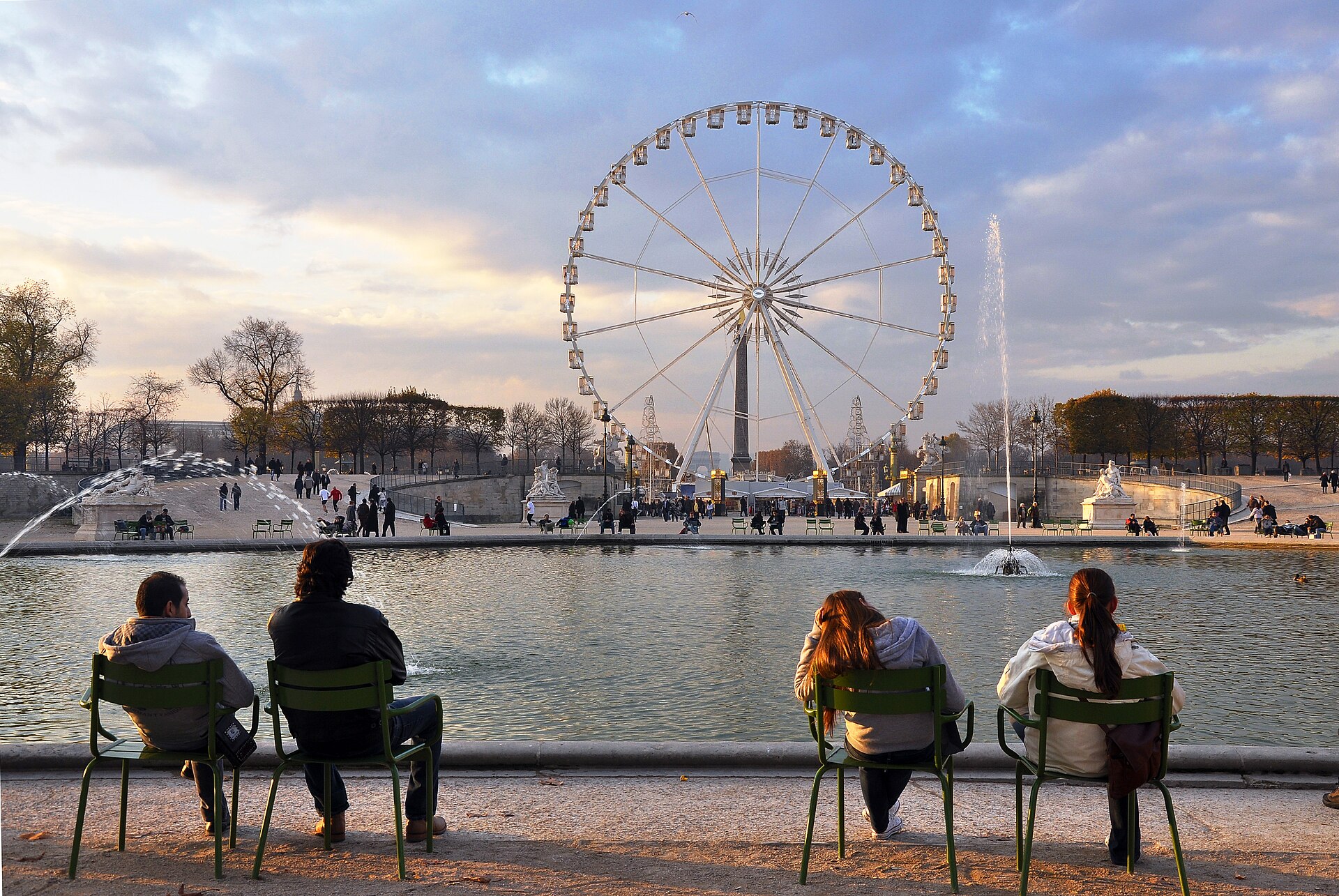 People sitting on green metal chairs around the octagonal basin in the Jardin des Tuileries at sunset