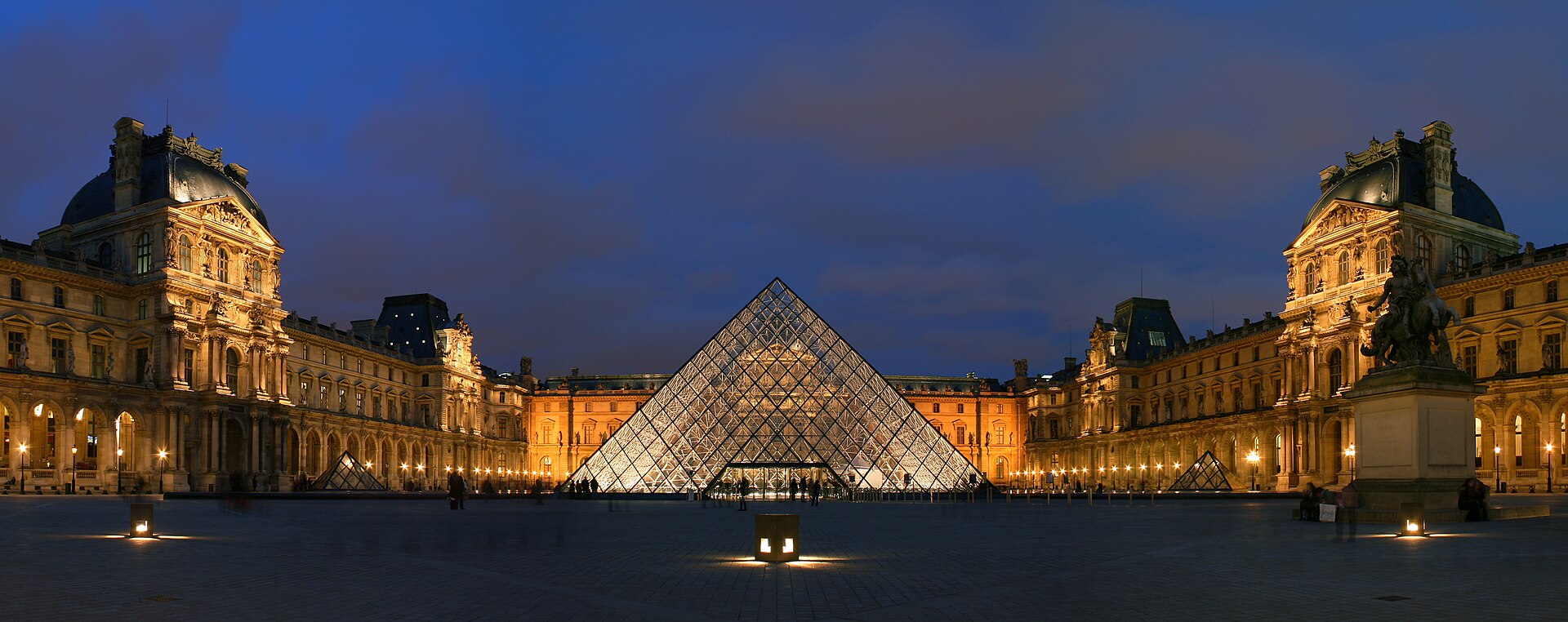 The Cour Napoleon at the Louvre at dusk, with the glass pyramid lit from within and the palace wings floodlit around it