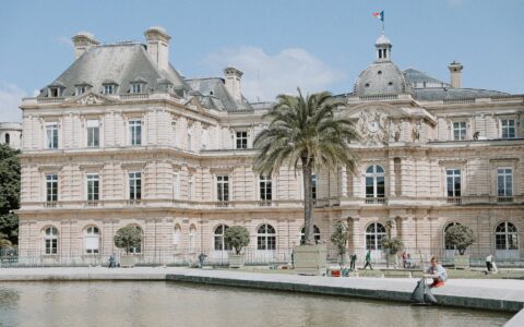 The Luxembourg Palace with its central dome and French flag seen across a pond, with a palm tree in a planter on the terrace
