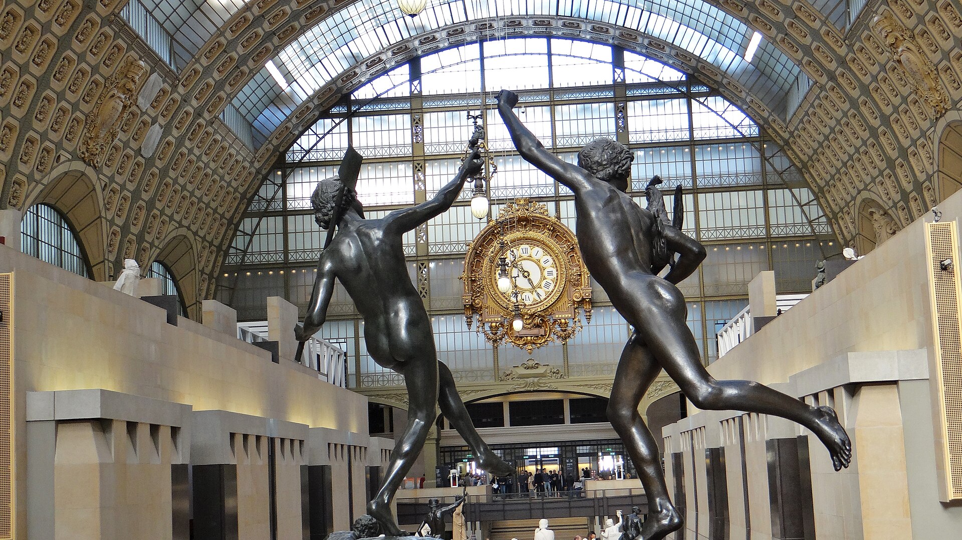 The great hall of the Musee d'Orsay with its glass barrel vault, gilded station clock and bronze sculptures in the foreground
