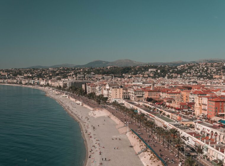 Aerial view of the curving pebble beach and turquoise water of the Baie des Anges in Nice, with the city and hills behind
