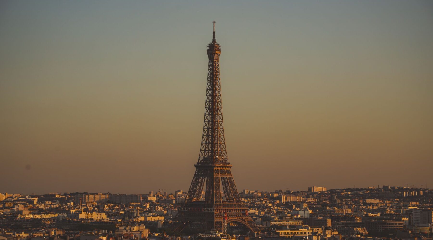 The Eiffel Tower rising above the Paris rooftops at dusk under a warm golden sky