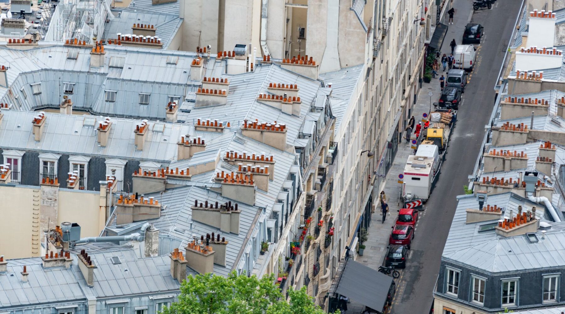 A high view over Paris rooftops with zinc roofs, terracotta chimney pots and a narrow street below