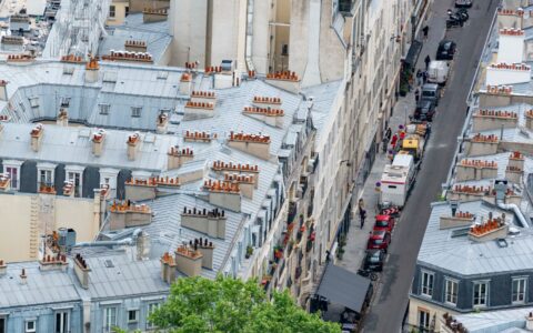 A high view over Paris rooftops with zinc roofs, terracotta chimney pots and a narrow street below