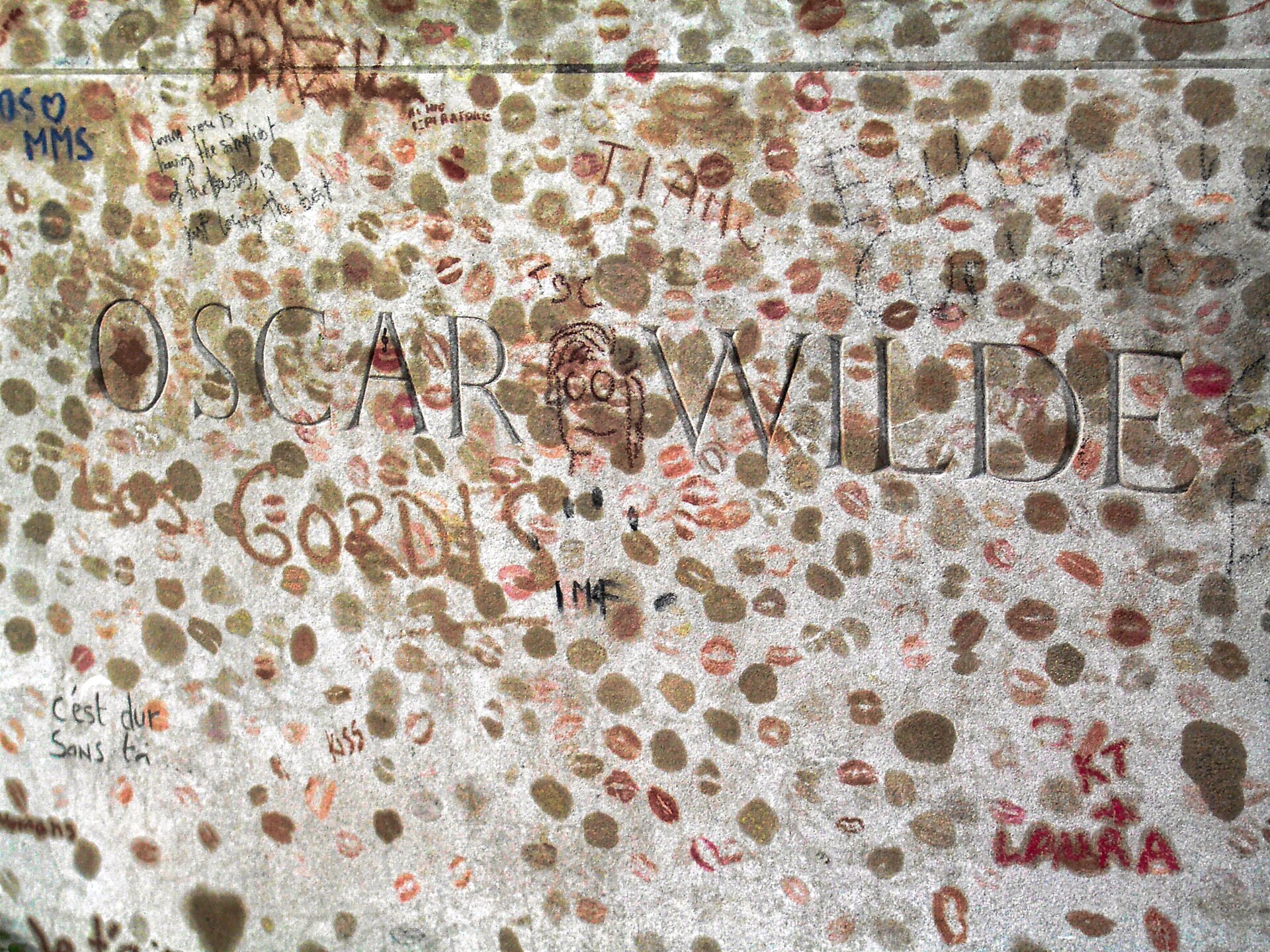 The stone of Oscar Wilde's tomb carved with his name and covered in hundreds of lipstick kisses and scrawled messages