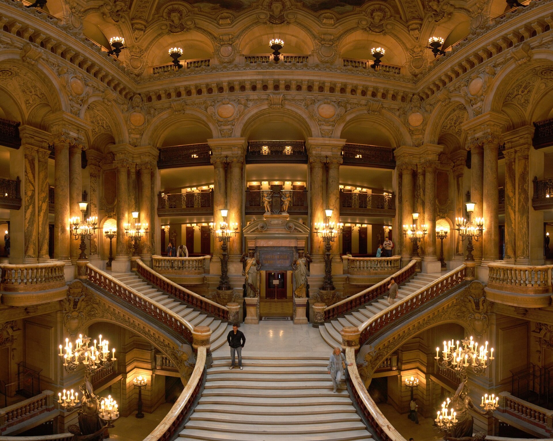 The grand staircase of the Palais Garnier opera house in Paris, in coloured marble under a vaulted painted ceiling and chandeliers