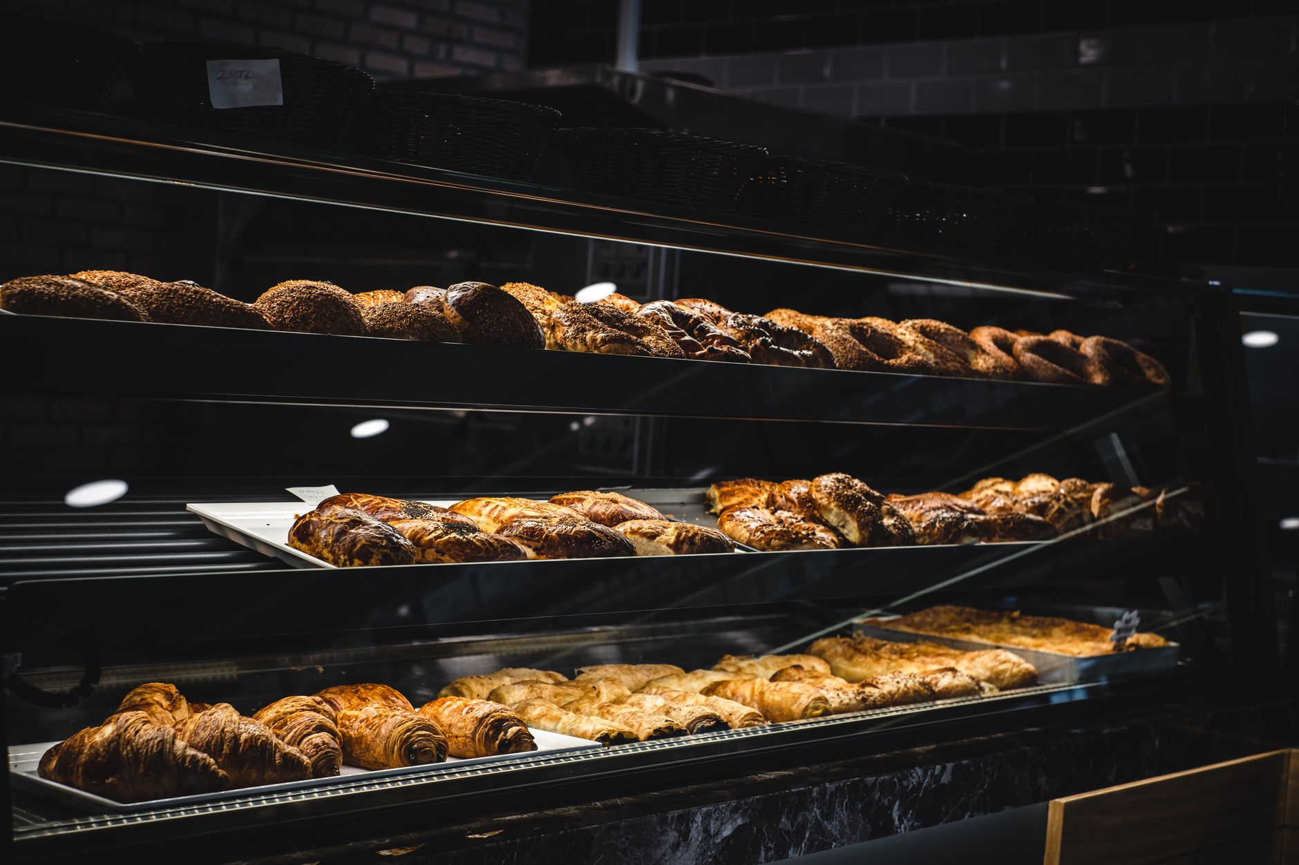 A bakery display case with trays of croissants, pains au chocolat and loaves under warm light