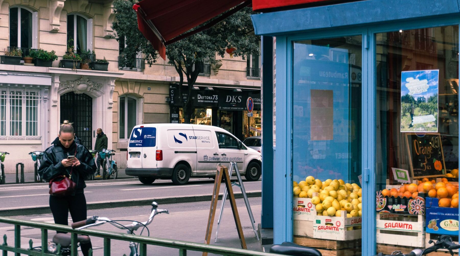 A blue-framed greengrocer's shop in Paris with crates of lemons and oranges on the pavement and a chalked price board