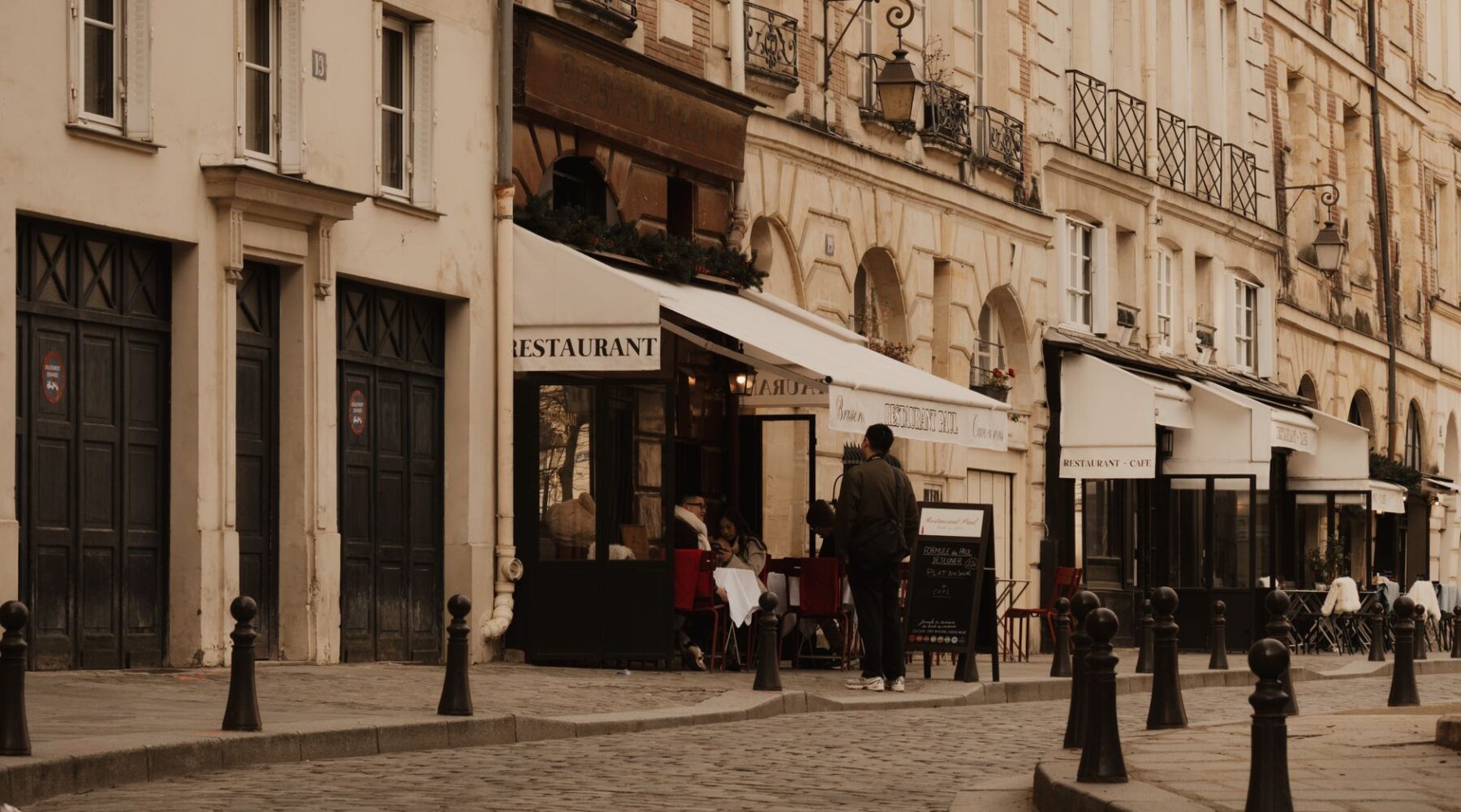 A quiet cobbled Paris street with restaurant awnings and cafe terraces in warm afternoon light