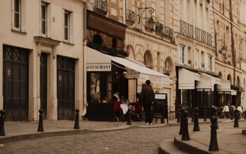 A quiet cobbled Paris street with restaurant awnings and cafe terraces in warm afternoon light