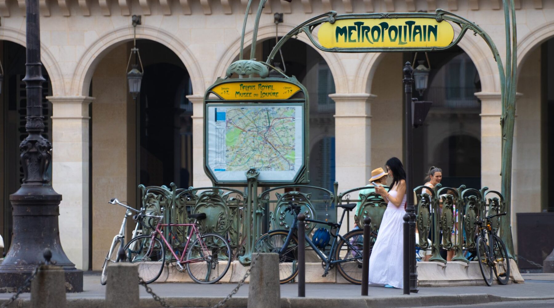 The Art Nouveau Metropolitain entrance at Palais Royal-Musée du Louvre with the network map, bicycles and passers-by
