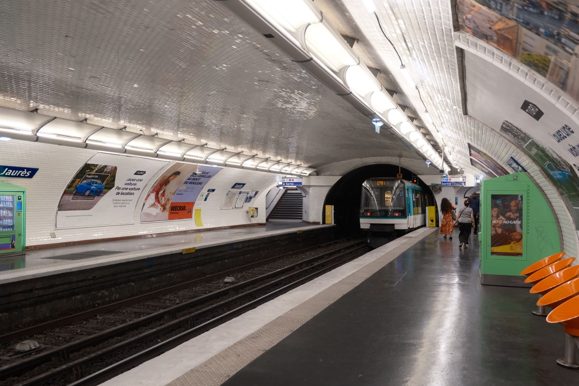 A train arriving at Jaurès station on the Paris Metro, with white tiled vaulting and orange platform seats