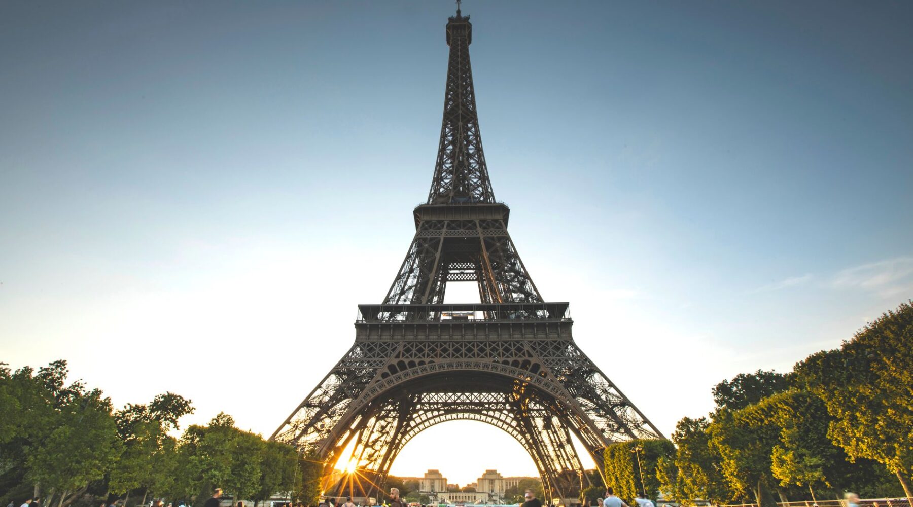 Visitors gathered on the grass of the Champ de Mars below the Eiffel Tower at sunset