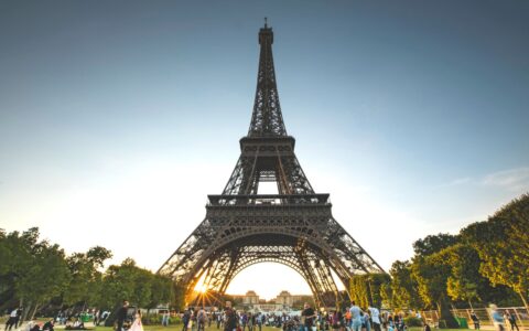 Visitors gathered on the grass of the Champ de Mars below the Eiffel Tower at sunset