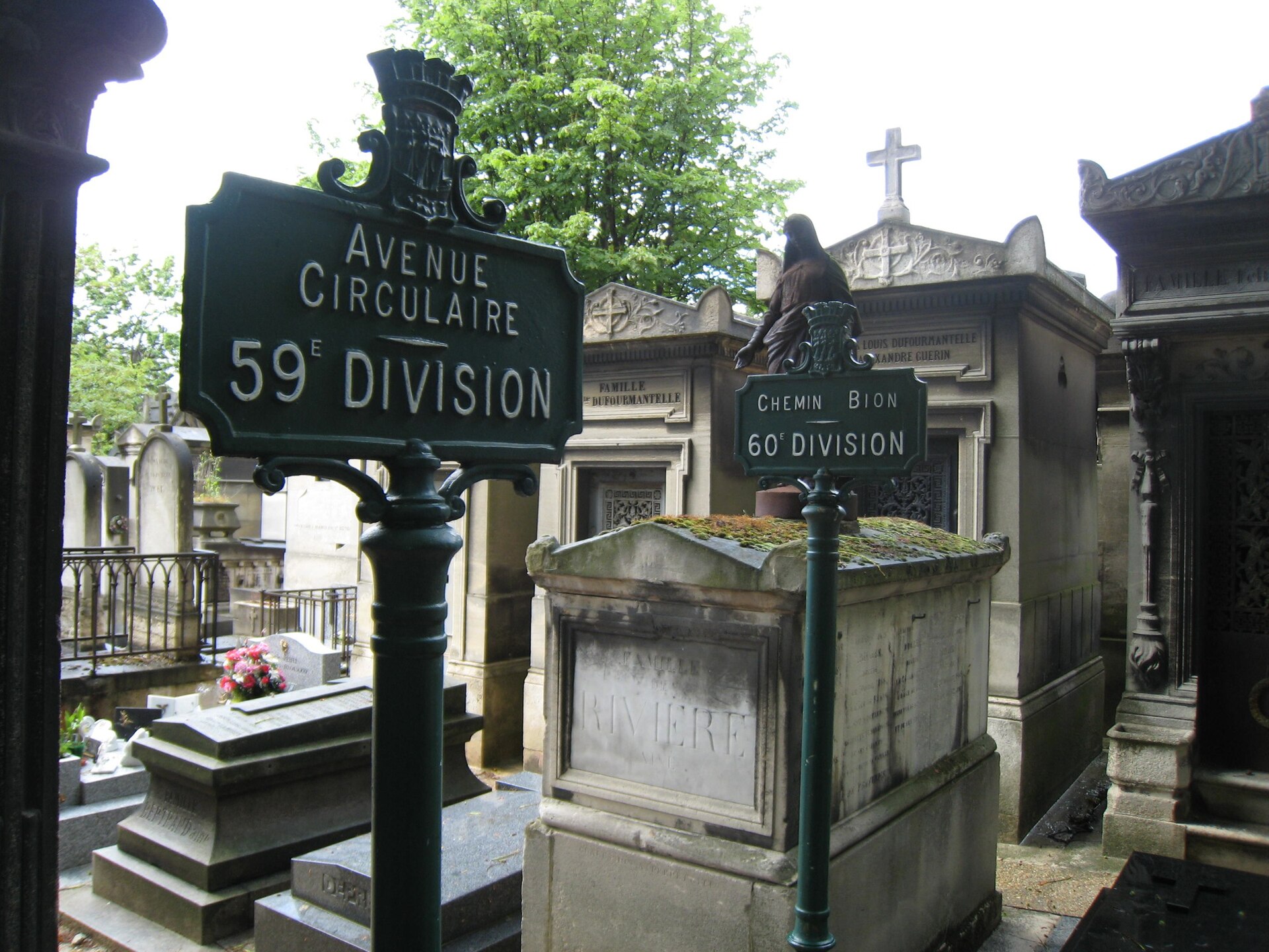 Cast-iron street signs reading Avenue Circulaire and Chemin Bion among the stone tombs of Pere Lachaise cemetery in Paris
