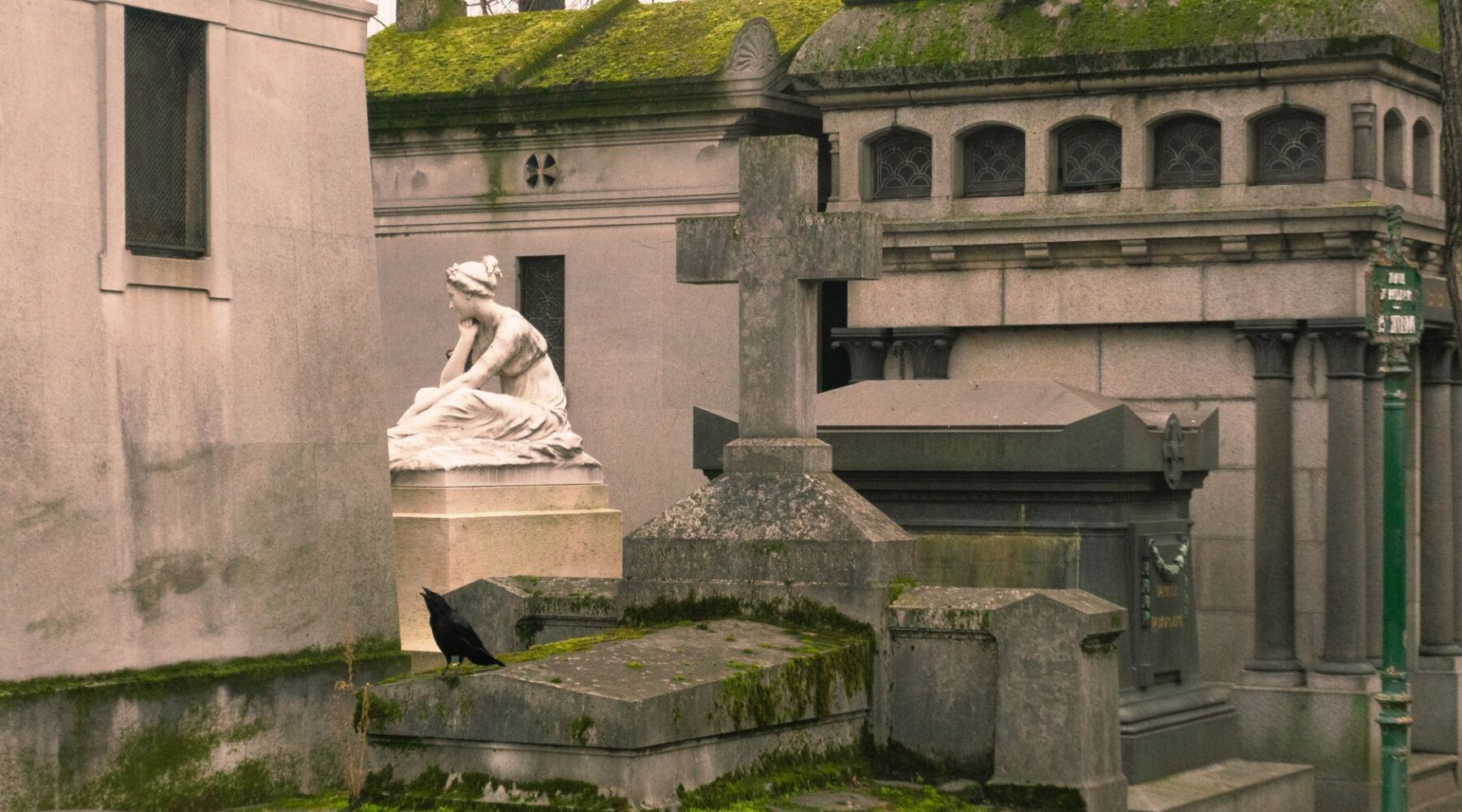 Moss-covered family chapels and a white marble mourning statue on a grave at Père Lachaise Cemetery