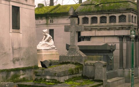 Moss-covered family chapels and a white marble mourning statue on a grave at Père Lachaise Cemetery