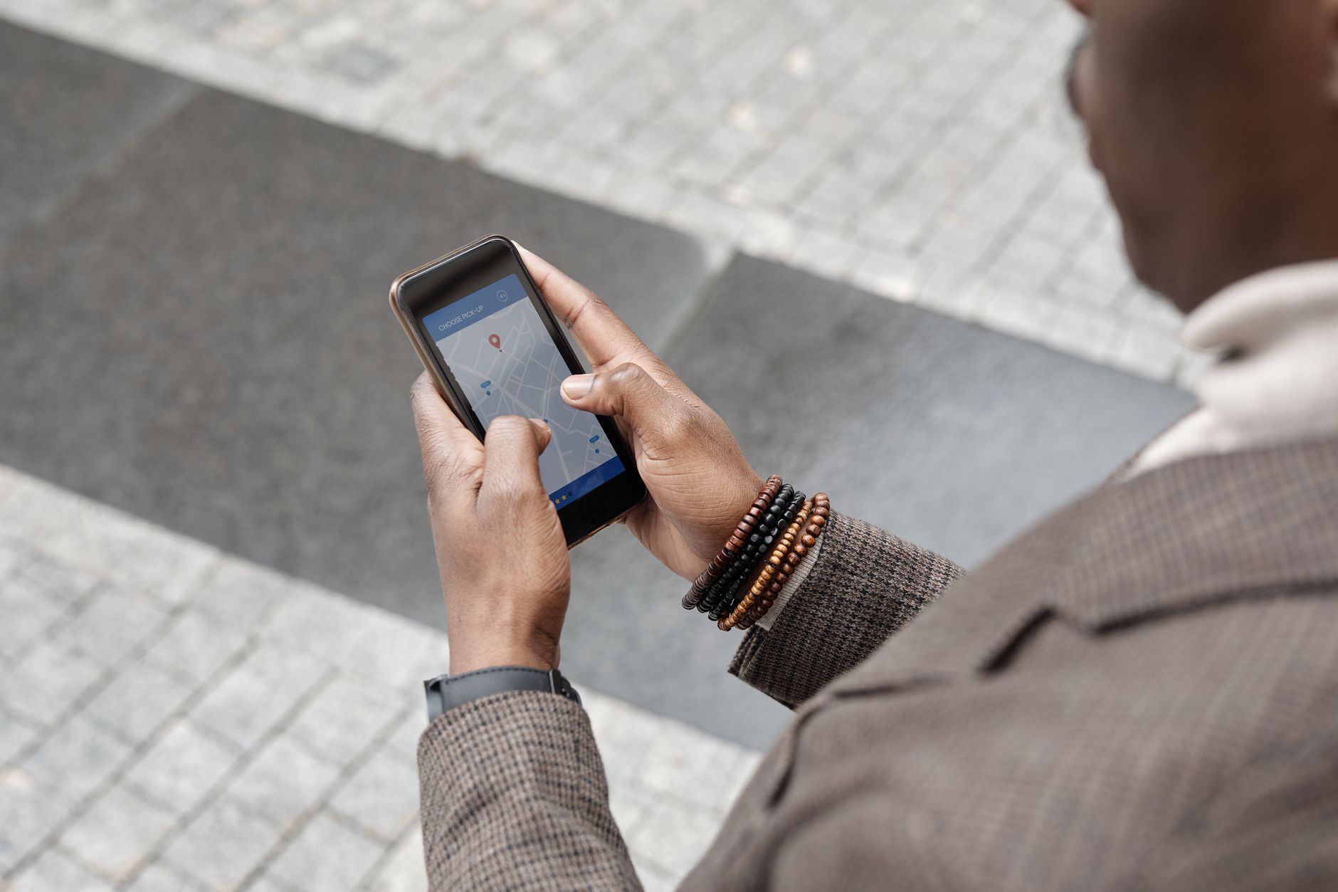 Close-up of a person holding a smartphone showing a map and pick-up location app while standing on a paved street