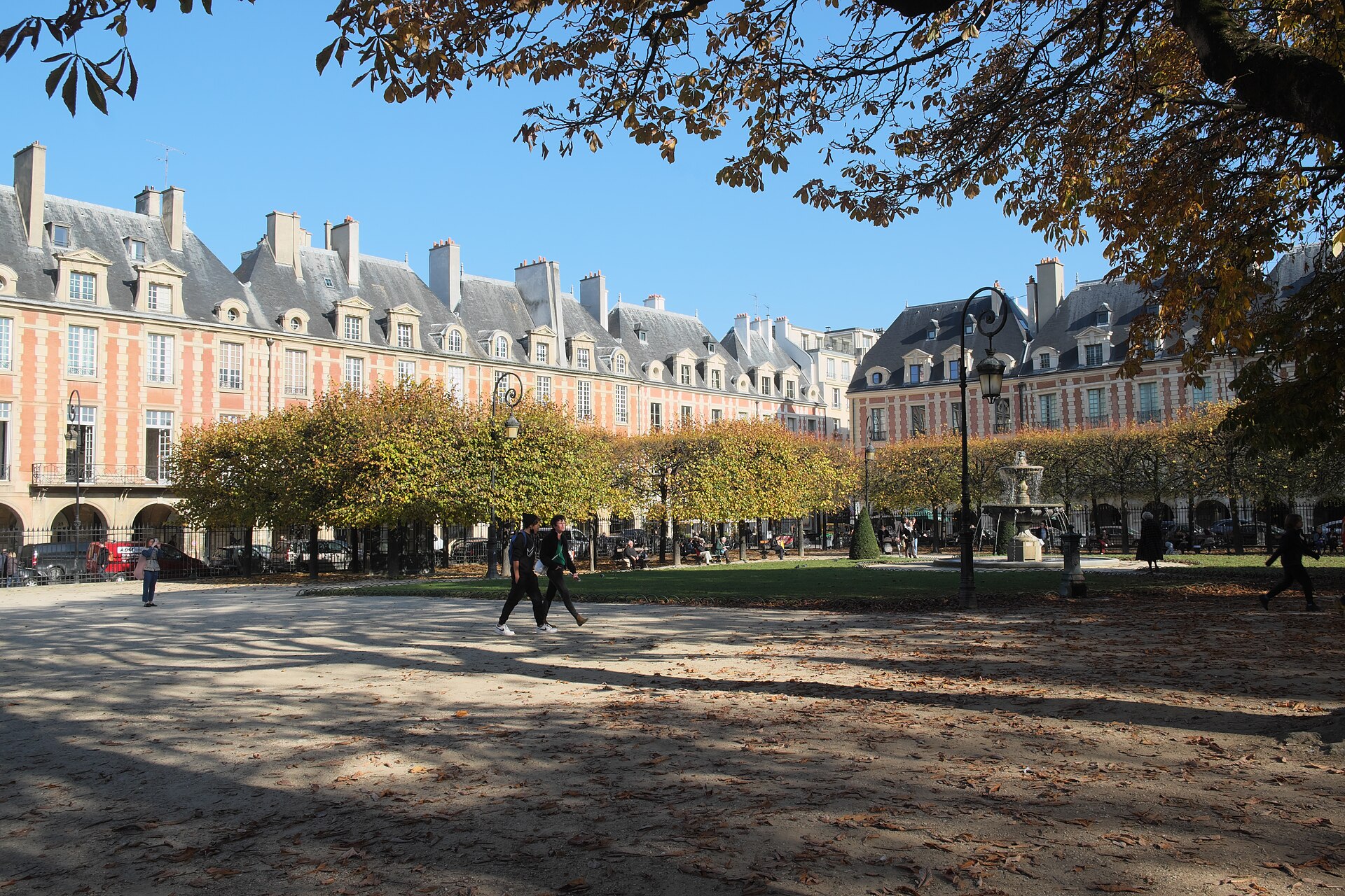 The brick and stone arcaded facades of the Place des Vosges in Paris seen across the gravel and lawns of its central garden in autumn