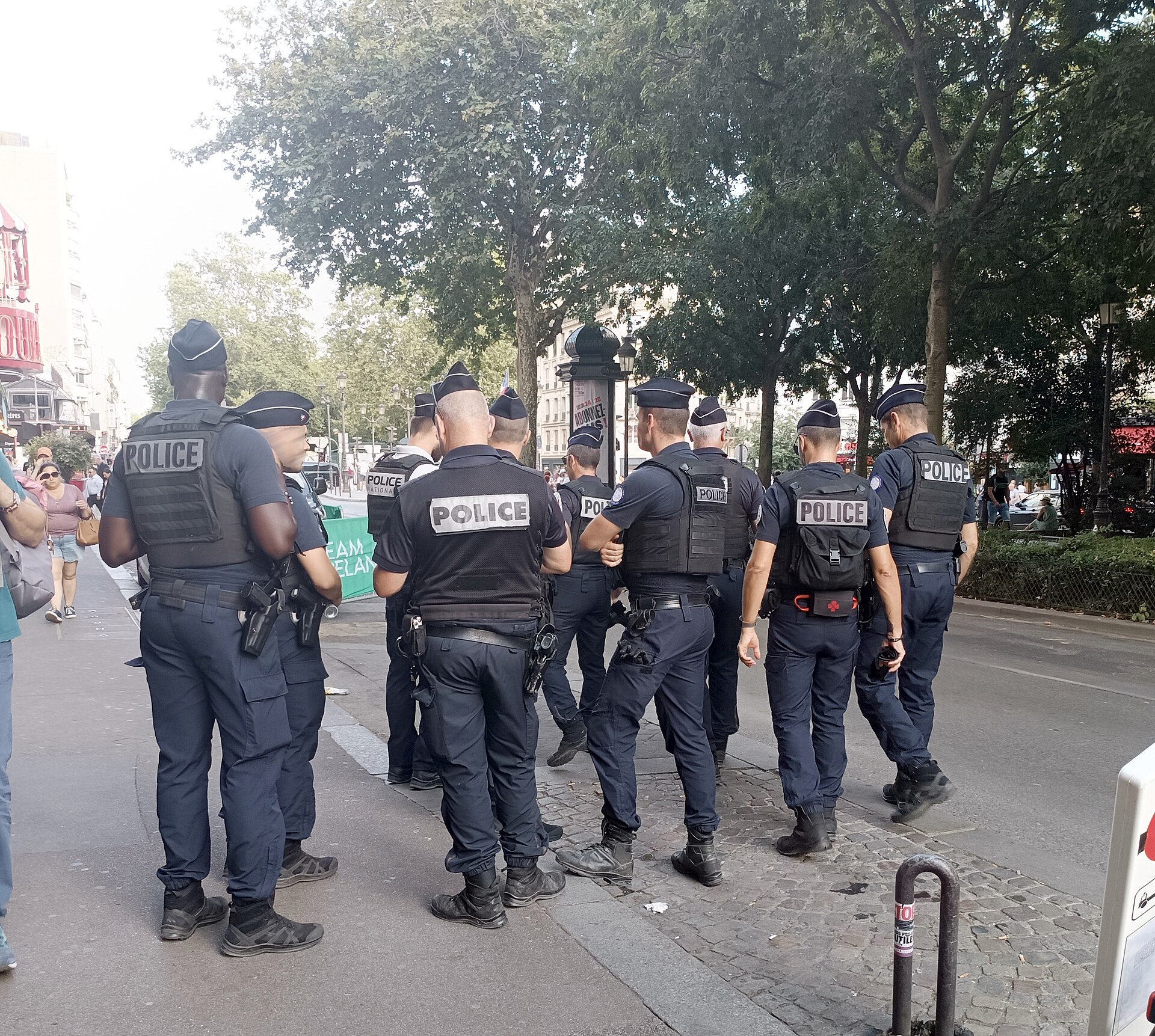 A group of French Police Nationale officers in uniform and body armour standing on a tree-lined Paris boulevard