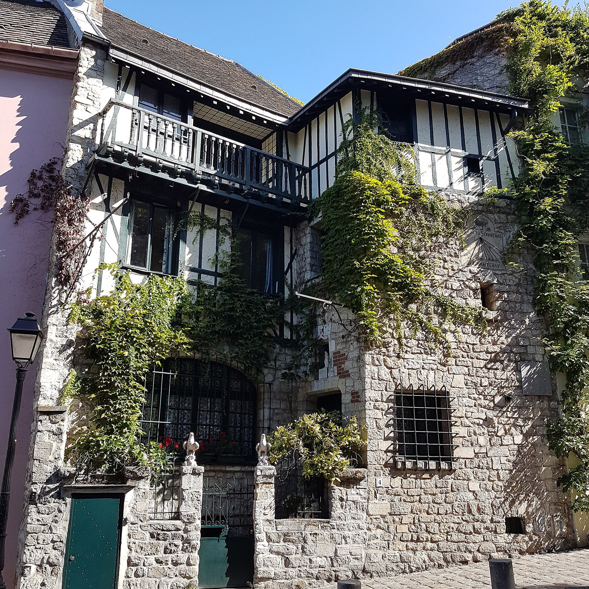 A half-timbered stone house covered in ivy on Rue de l'Abreuvoir in Montmartre, with a sundial on the wall