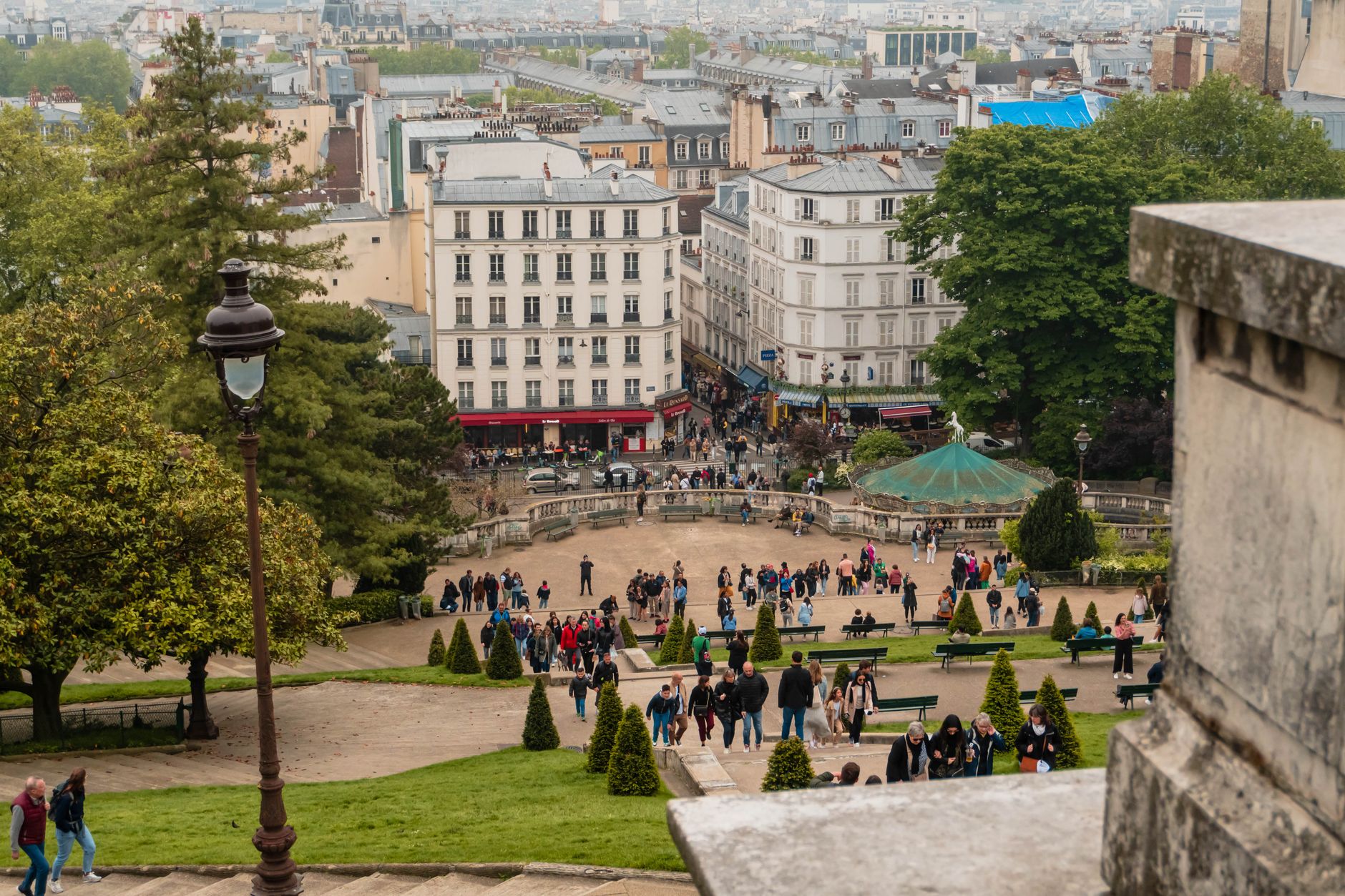 View down the terraced gardens and steps below Sacré-Cœur towards the Montmartre carousel and the rooftops of Paris