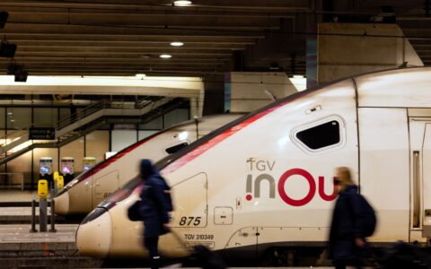 Travellers with suitcases walking past the nose of a TGV INOUI high-speed train at a Paris station platform