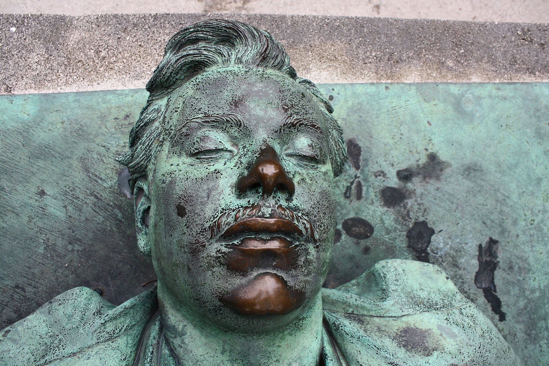 Close-up of the green-patinated bronze face of Victor Noir's effigy lying on his tomb, with the lips and nose rubbed shiny