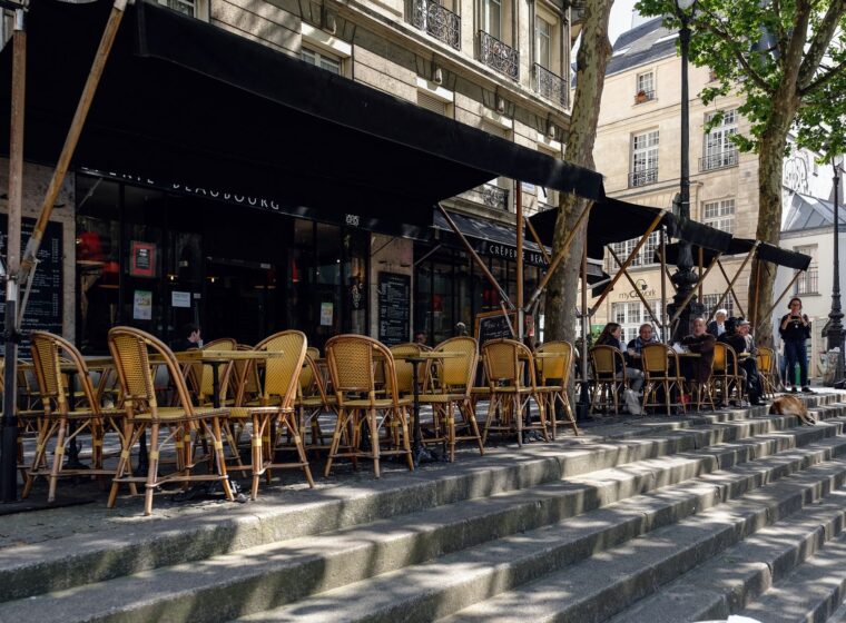 Rattan cafe chairs and tables under black awnings on a sunny Paris pavement terrace