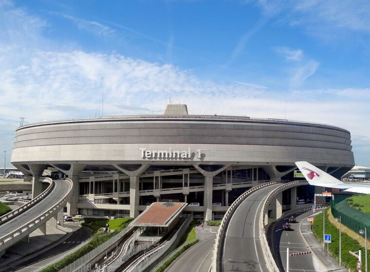 The round concrete Terminal 1 building at Charles de Gaulle airport on its pillars, with curving approach roads below and a blue sky