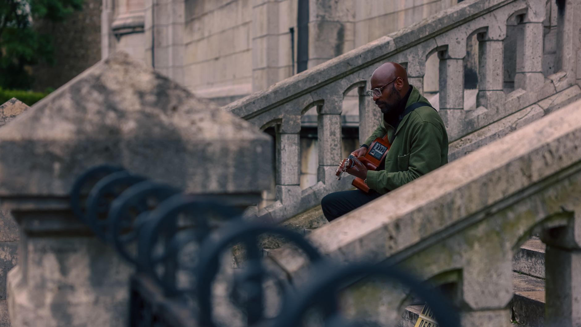 A man in a green jacket playing an acoustic guitar on the stone stairs below the Sacré-Cœur in Montmartre