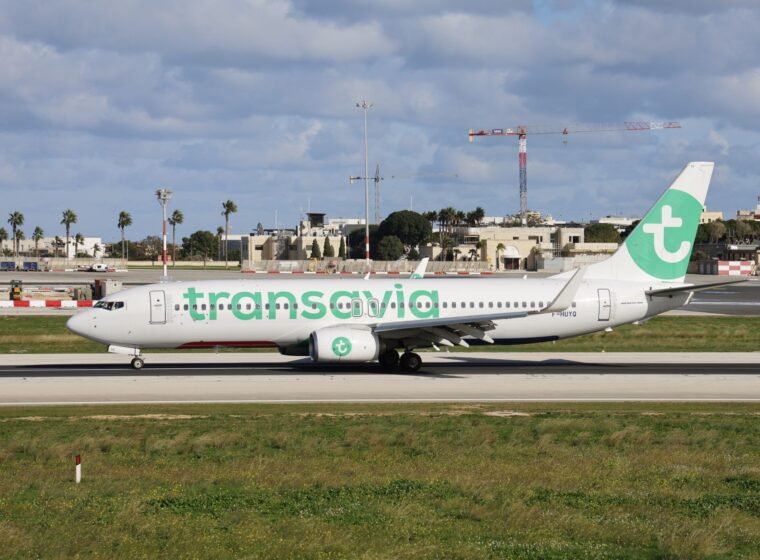 A white Transavia Boeing 737 with green lettering and a green tail logo on a runway under a cloudy sky
